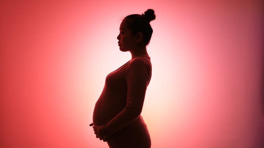 A pregnant woman in silhouette stands against a red and white background.