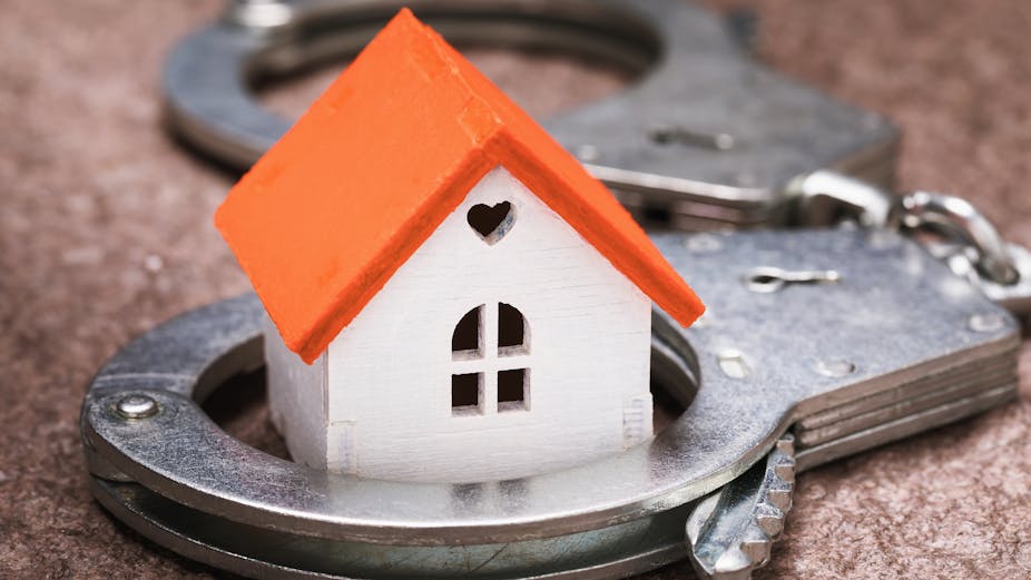 A small toy house is juxtaposed with a pair of handcuffs. 